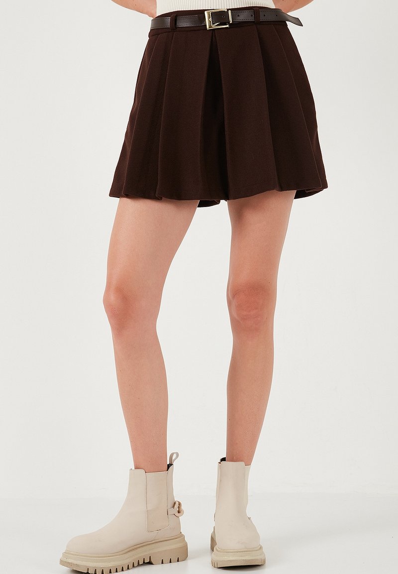 Bruine geplooide rok met een fitted tailleband en een contrasterende bruine riem met een gouden gesp. G gedragen met beige enkellaarsjes.