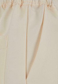 Beige bomullsstoff med en jevn tekstur, med en sidelomme og elastisk midje. Faltene gir ekstra dimensjon til designet.