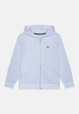 Haut de survêtement zippé bleu clair avec une poche kangourou, des poignets côtelés et un logo Lacoste ton sur ton. Tissu doux avec une texture lisse.