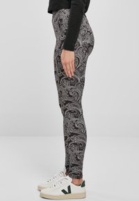 Crne tajice s složenim bijelim paisley uzorkom, visoki struk, rastezljivi materijal, u kombinaciji s bijelim tenisicama s zelenim detaljima.