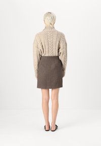 Suéter de punto beige con un cuello alto, combinado con una falda corta de cuadros marrón. Unos sencillos zapatos negros tipo slip-on completan el atuendo.