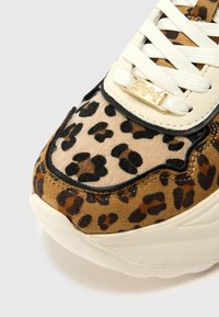 Sapatilhas com padrão de leopardo, combinando camurça bege e material liso; apresentam atacadores brancos e um detalhe em logo dourado na lingueta.