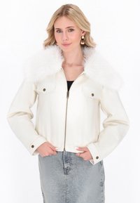 Giacca in ecopelle bianca con colletto soffice bianco, chiusura con zip, due tasche frontali e bottoni, abbinata a una gonna di jeans.