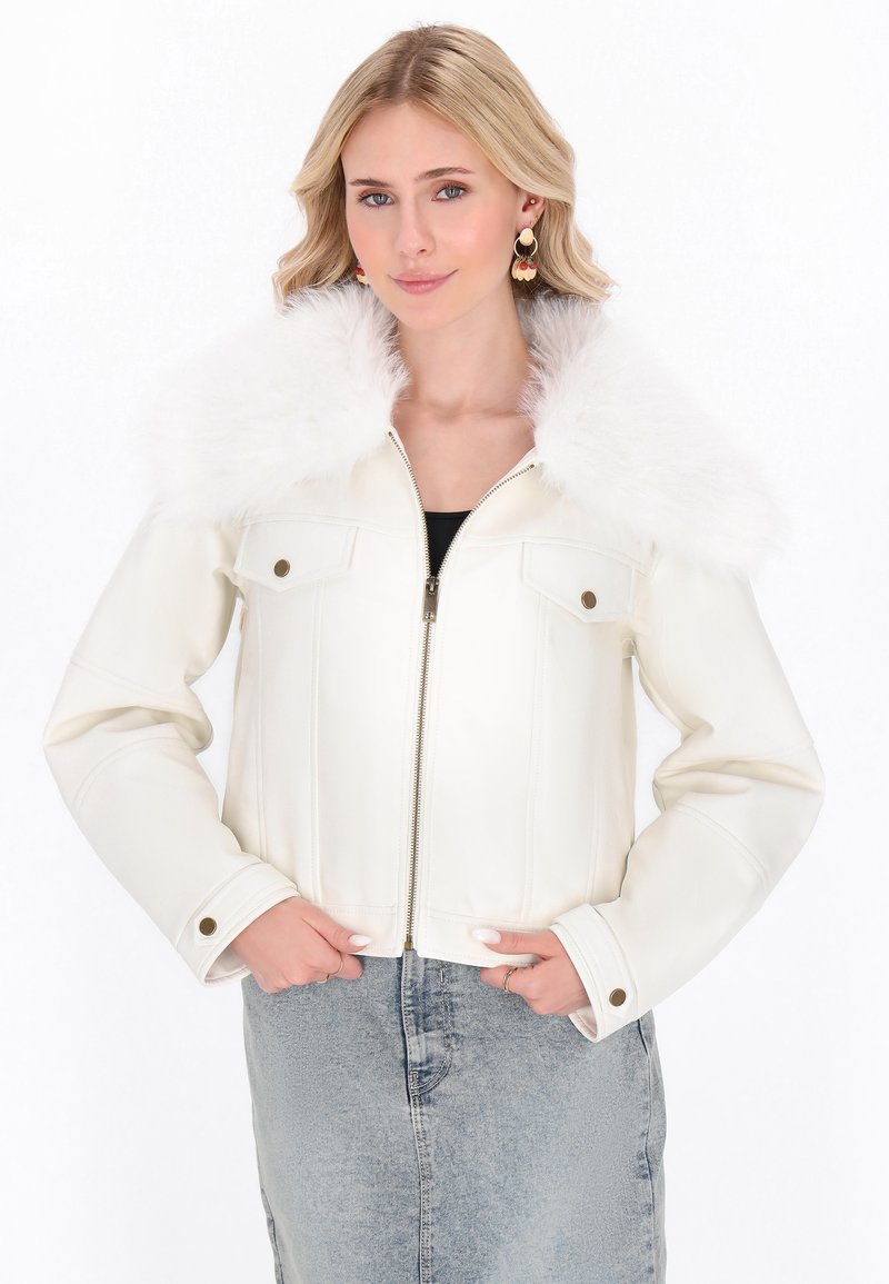 Giacca in ecopelle bianca con colletto soffice bianco, chiusura con zip, due tasche frontali e bottoni, abbinata a una gonna di jeans.