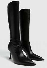 Czarne skórzane botki na wysokim obcasie z wąskim noskiem, dopasowanym cholewką i bocznym zamkiem. Gładka tekstura z przeszyciami wzdłuż szwów.