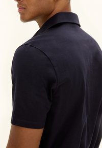 Navy short-sleeve polo shirt with a collar, made of smooth fabric. Features a clean design with minimal stitching and a subtle texture.