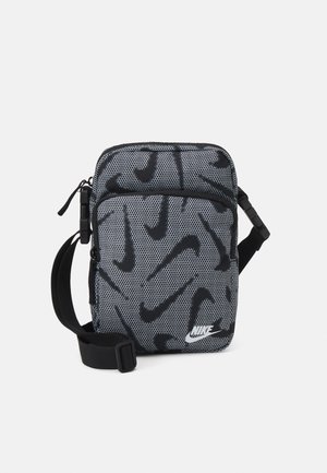 Mała czarna i szara torba na ramię Nike z wieloma czarnymi logo swoosh, regulowanym paskiem i przednią kieszenią na zamek, pokazana na prostym tle.
