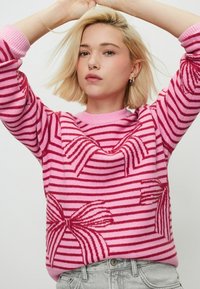 Pull en tricot rose avec des rayures horizontales et des motifs de nœuds, doté d'un col rond et de poignets côtelés. Texture douce, design décontracté.