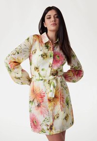 Kwiatowa sukienka koszulowa z lekkiego materiału, w różowe, żółte i zielone wzory kwiatowe, z guzikami z przodu i związanym paskiem w talii.