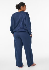 Navy blue lounge setti, jossa on pitkähihaiset, leveähihaiset paidat ja rento istuvuus housut, joissa on sivutaskut. Setti on valmistettu pehmeästä, teksturoidusta kankaasta.