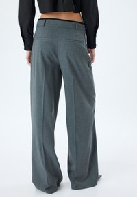 Graue weit geschnittene Hosen mit maßgeschneiderter Gestaltung, ausgestattet mit Gesäßtaschen und einem glatten, strukturierten Stoff. Der Abschluss hat einen sauberen Saum.