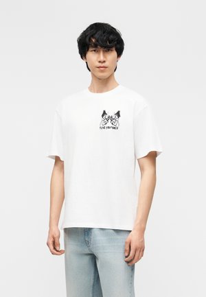 Noor mees kannab valget T-särki, millel on musta joonega joonistus kahest figuurist ja rinnal kiri „find yourself“, sobitatuna heledate teksadega.