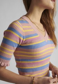 Barevný žebrovaný pletený top s růžovými, modrými a žlutými pruhy. Design s výstřihem do V, krátké rukávy a detail volánkového lemu.