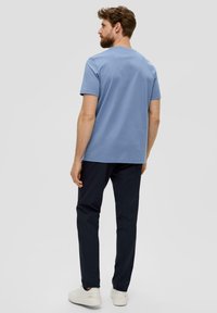 Hellblaues Baumwoll-T-Shirt mit kurzen Ärmeln und Rundhalsausschnitt, kombiniert mit dunkelblauen Hosen und weißen Sneakers, von hinten präsentiert.