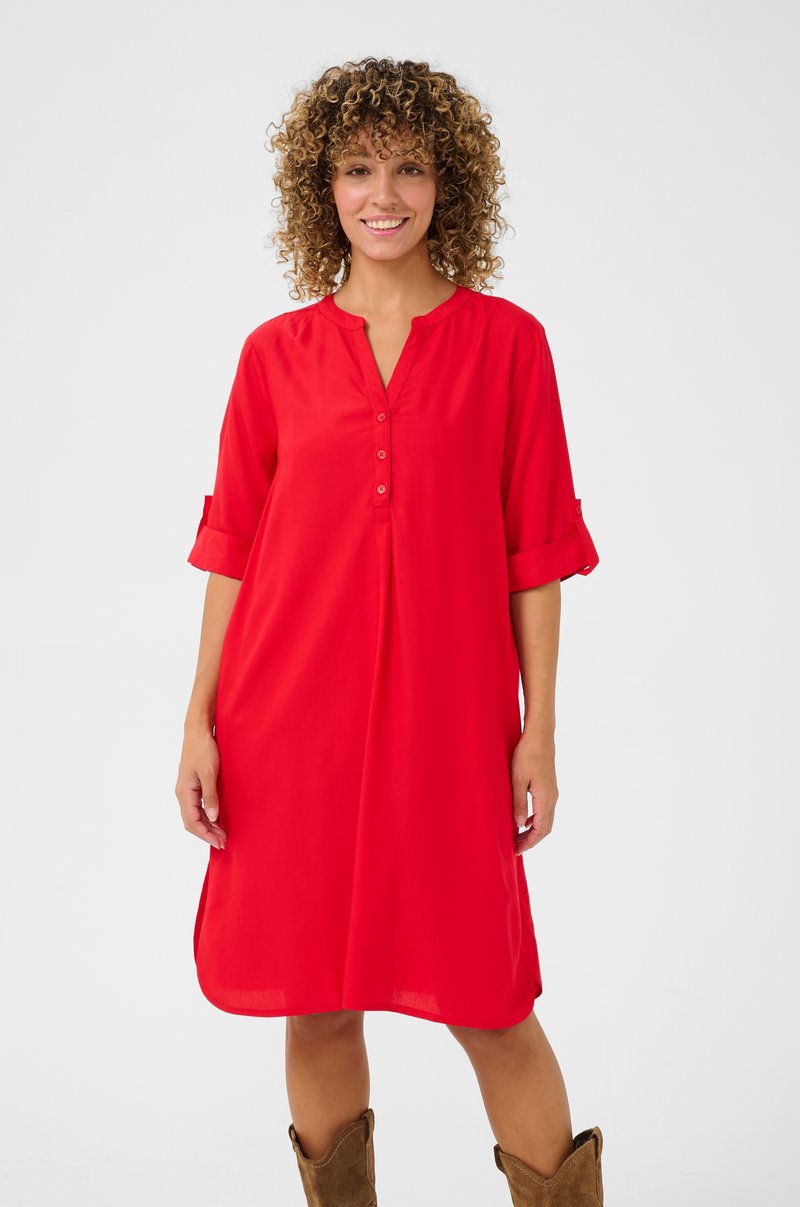 Robe rouge avec un décolleté en V, avant à boutons et manches roulées. Conçue en tissu léger, elle présente une coupe ample qui arrive au-dessus des genoux.