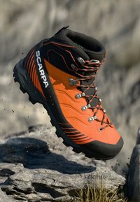 Stivale da mountain con un design arancione e nero, caratterizzato da una superficie testurizzata, occhielli in metallo e una suola robusta per la trazione.