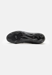 Black soccer cleat sole with recessed studs, textured grip patterns, and smooth accents, designed for traction on turf surfaces.