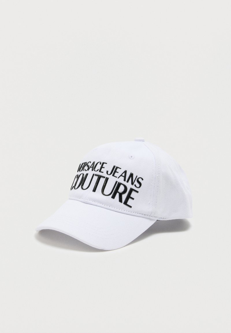 Λευκό καπέλο μπέιζμπολ με κυρτή γείσο, μαύρο κεντημένο κείμενο "VERSACE JEANS COUTURE" στο μπροστινό μέρος, πάνω σε απλό φωτεινό φόντο.