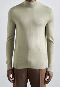 Světlý zelený rolák z měkkého pleteného materiálu. Přiléhavý střih s dlouhými rukávy, žebrovanými manžetami a lemem.