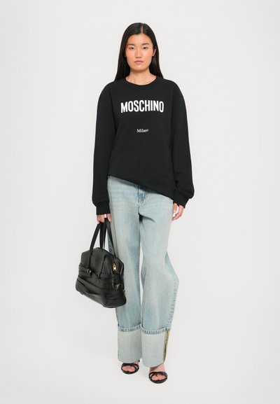 Sudadera negra con el logo blanco "Moschino Milano"; jeans de pierna ancha en azul claro con detalle de dobladillo; bolso negro; sandalias negras.