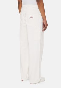 Pantalones de algodón blancos de pierna ancha con dos bolsillos traseros y un pequeño logo en el bolsillo derecho. Cuenta con una cintura alta y un ajuste casual.