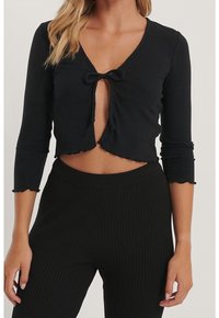 Svart ribbad crop top med trekvartsärmar, med en djup V-ringning och en frontknutning. Sömmen är lätt fransad för textur.