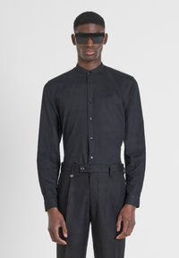 Camicia nera a manica lunga con colletto abbottonato e dettagli di logo discreti, abbinata a pantaloni neri con cintura e dettagli a clip.