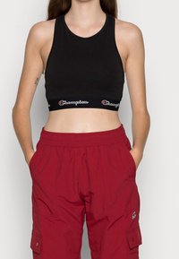 Czarny bawełniany stanik sportowy z szeroką elastyczną taśmą z logo "Champion". Połączony z luźnymi czerwonymi spodniami cargo.