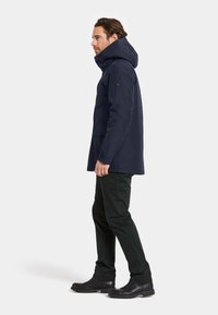 Marinblå vattentät parkas med huva, som har framfickor, knäppt ärm och en elegant, strömlinjeformad design.