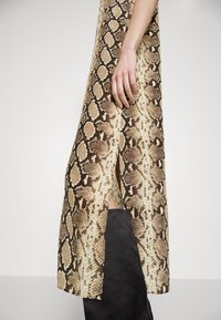 Python-print kjole med en delvis sideslids, lavet af glat stof med en lys beige- og brun farveskala. Sorte detaljer i bunden.