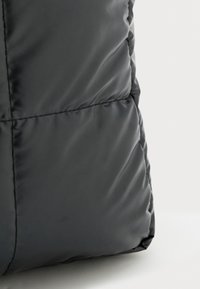 Gros plan sur un tissu rembourré noir matelassé avec des coutures horizontales et une texture lisse sur un fond clair.