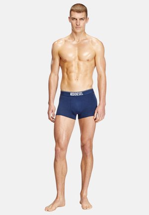Navy blue boxer briefs with a white Diesel logo waistband, made from a smooth fabric. Fitted design, mid-thigh length. Model standing barefoot.