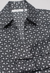 Chemise à motifs noir et blanc avec un design géométrique, un col pointu et une texture de tissu au fini lisse. Étiquette Eterna visible.