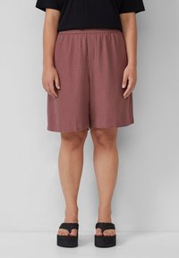 Helle rosa, knielange Shorts mit elastischem Bund; aus weichem Stoff mit lässiger Passform; kombiniert mit schwarzen Plateausandalen.