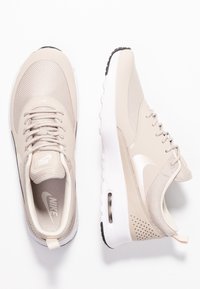 Béžové tenisky Nike Air Max z prodyšné síťoviny a syntetických materiálů, zaoblená špička, šněrování a bílá podrážka s černými akcenty.