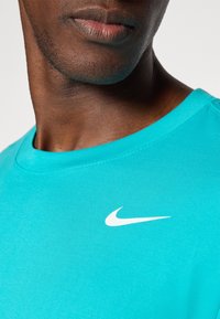 Turkusowa koszulka z bawełny z okrągłym dekoltem, z białym logo Nike w kształcie łyżwy na piersi, gładką fakturą i krótkimi rękawami.