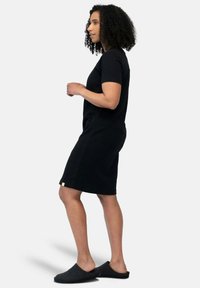 Abito nero a maniche corte in tessuto morbido con una vestibilità rilassata, caratterizzato da un orlo leggermente sopra il ginocchio e un piccolo dettaglio dell'etichetta sul fondo.