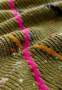 Knitted textile features an olive green base with vibrant pink and orange stripes, interspersed with colorful specks throughout the texture.