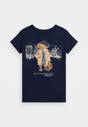 T-shirt de algodão azul-marinho com uma gráfica de um urso num casaco bege, chapéu estampado, colete de fato, e a segurar uma bolsa, com uma paisagem urbana ao fundo.