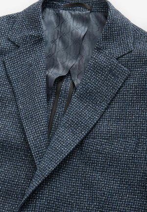 Blazer blu navy con texture e motivo intrecciato, taschino sul petto singolo e fodera grigia liscia con un sottile design geometrico all'interno.