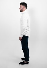 Witte blouse met lange mouwen, marineblauwe broek en zwarte instapschoenen. De blouse heeft een rechte kraag en een getailleerd ontwerp, waarin klassieke elementen worden getoond.