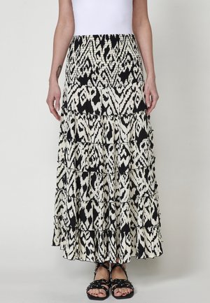 Jupe maxi à motifs noir et blanc avec un design à étages, fabriquée en tissu léger. Ourlet volanté et taille smockée. Portée avec des sandales à lanières.