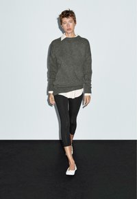 Grå tröja över en vit skjortkrage, kombinerad med svarta leggings och vita skor. Mjuk textur med en avslappnad passform och lager-på-lager-look.