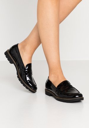 Sorte lakskind-loafers med chunky sål, båret på bare fødder, vist på en glat lys overflade.