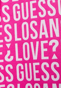 Helle pinkfarbene Stoff mit fettem weißen Text, auf dem die Worte "GUESS", "LOS ANGELES" und "LOVE?" deutlich zu sehen sind.