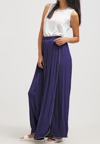 Top blanco sin mangas con costuras decorativas, combinado con una falda maxi fluida de color púrpura oscuro con detalles laterales y sandalias planas.