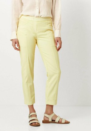 Yellow, slim-fit pants with a smooth texture and elastic waistband, paired with flat, strappy beige sandals.