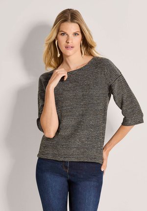 Blonde Frau mit großen goldenen Creolen, einem schwarz-weißen gestrickten Boatneck-Top mit Dreiviertelärmeln und dunkelblauen Jeans.
