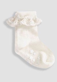 Weiße Baumwollsocke mit einer Spitze am Rippbündchen. Mit geprägten Sternen und Punkten an der Sohle für besseren Halt. Weicher Stoff und geripptes Design.