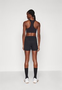 Svart sports-bh og shorts med en tettsittende design. Bh-en har racerback; shortsene er løse. Hvite sneakers og svarte sokker med detaljer.